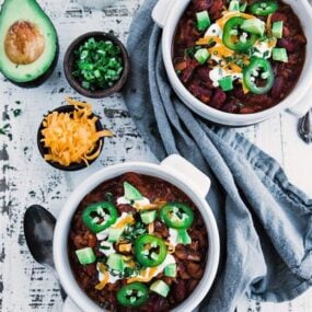 bowls of chili topped off with sour cream and avocados next to other toppings