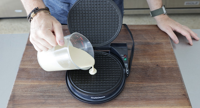 adding waffle batter to a hot waffle iron