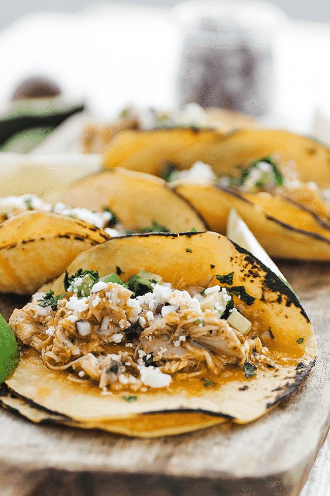 chicken tinga tacos with cheese and lime on a cutting board