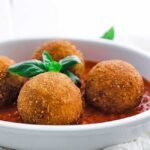 browned risotto arancini in a dish with tomato sauce and basil