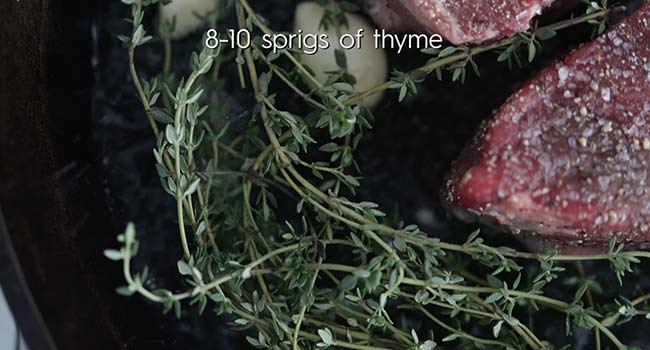 thyme and garlic in a pan with steak