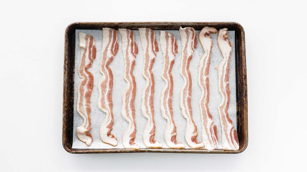 raw bacon on a sheet tray lined with parchment paper