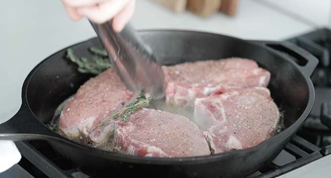 adding thyme and butter to a pan of searing pork chops