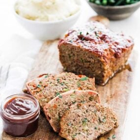 sliced meatloaf on a cutting board next to mashed potatoes and green beans