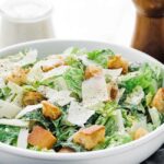 a caesar salad with dressing and parmesan cheese shavings