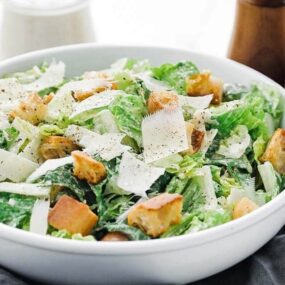 a caesar salad with dressing and parmesan cheese shavings