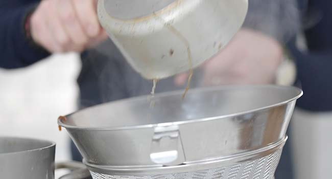 straining a beef stock through a chinois