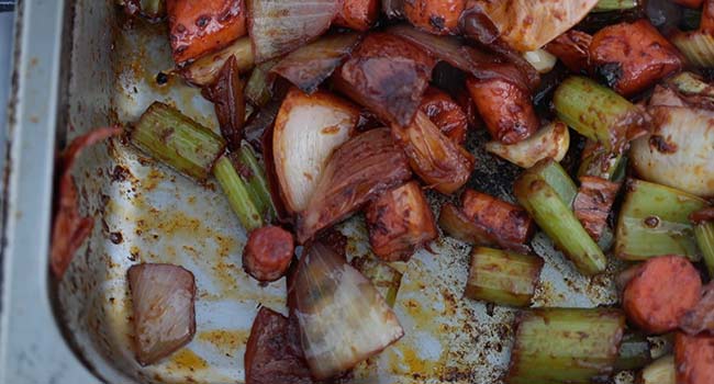 mixing tomato paste in with a pan of roasted vegetables