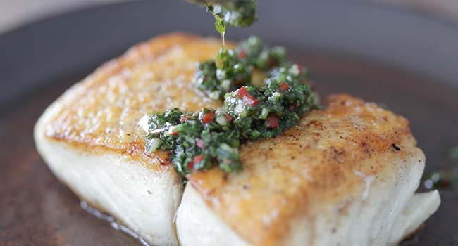 adding chimichurri sauce to cooked halibut