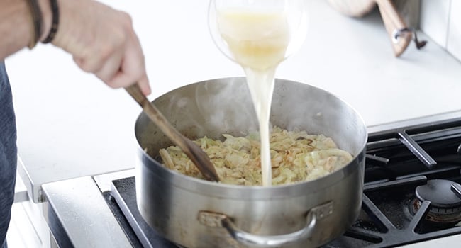 adding chicken stock to fried cabbage