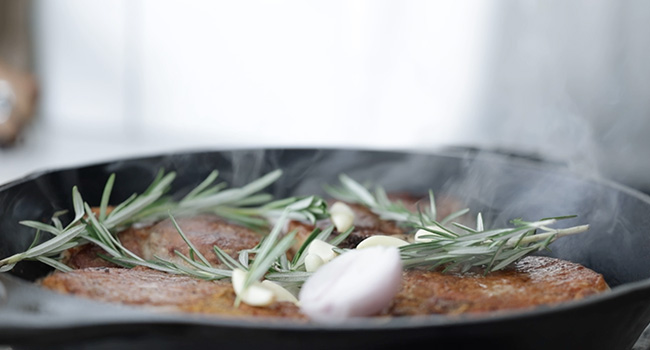 adding herbs and garlic to a pan with pork