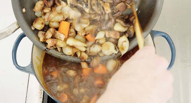 adding mushrooms and carrots to a pot