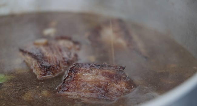 adding beef to a pot with beef stock