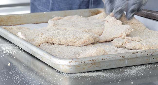 adding breaded pork to a sheet tray