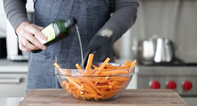 adding oil to a bowl of sweet potato fries