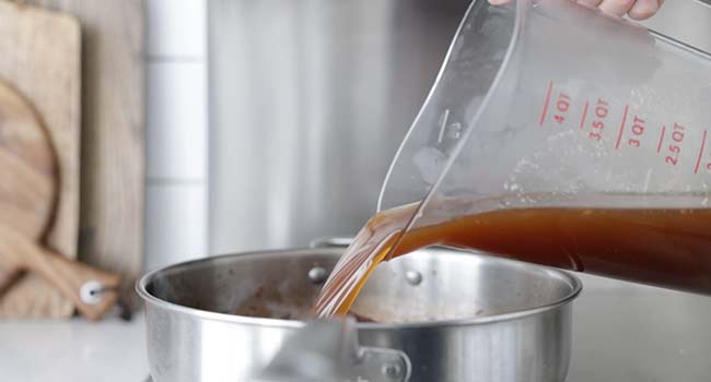 adding beef stock to a pot