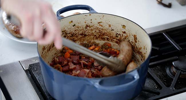 adding sausage to a pot of carrots and onions