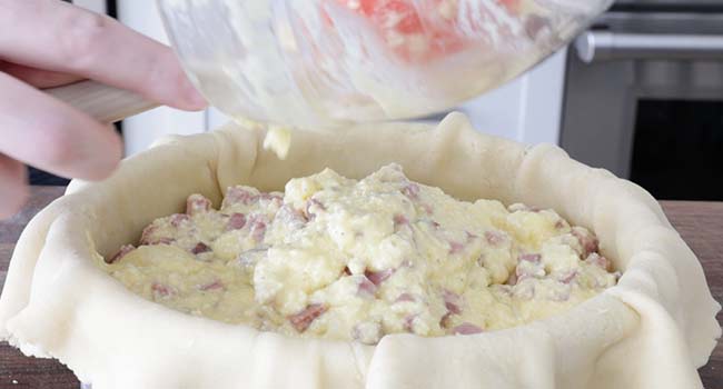 adding ham and eggs to a pan of dough