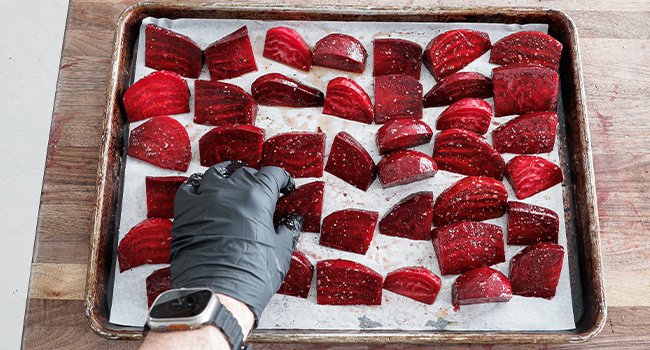 adding seaosned beets to a sheet tray lined with parchment paper