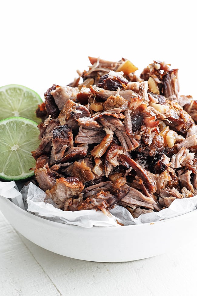 carnitas in a bowl with limes