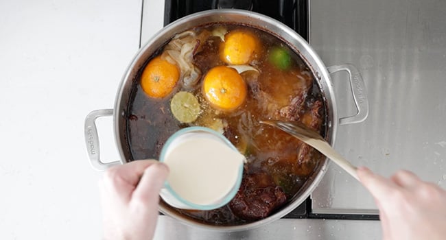 adding milk to carnitas with oranges and limes