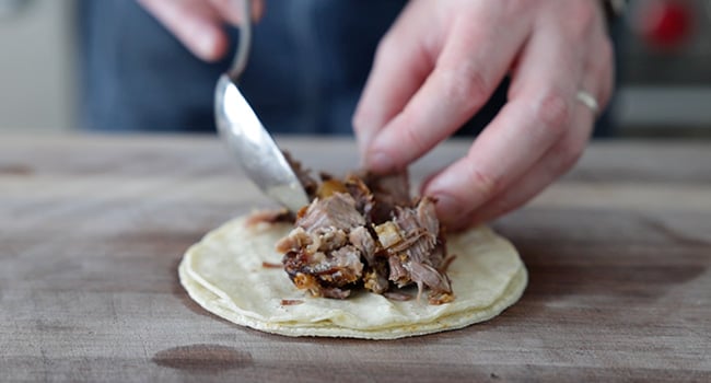 adding carnitas to corn tortillas