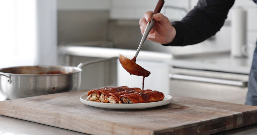 adding sauce onto enchiladas