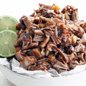 carnitas in a bowl with limes