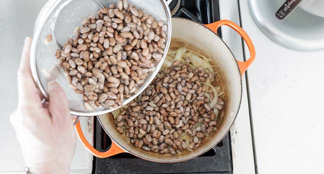 adding beans to a pot of onions