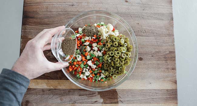 adding spices to a bowl of vegetables