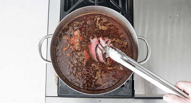 adding sliced beef to broth in a pot