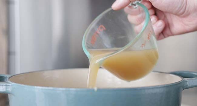 adding chicken stock to a pot