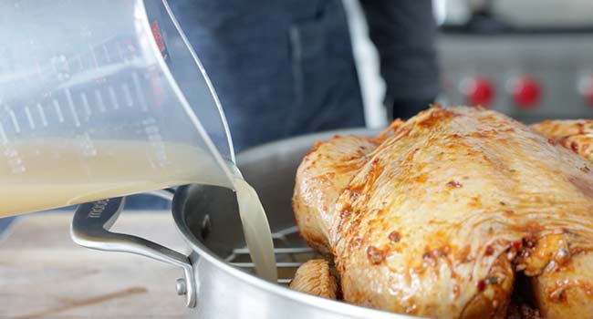 adding stock to a pot with chicken