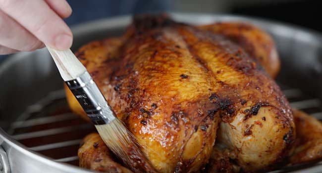 brushing a roasted chicken with a marinade