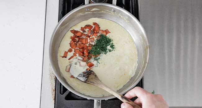 adding salmon and dill to a pot of cream