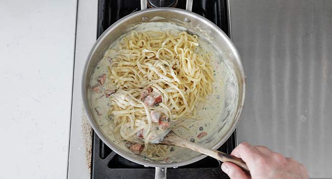 folding pasta into a pot of cream