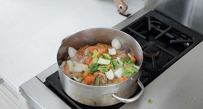 adding vegetables to a pan of chicken cooking