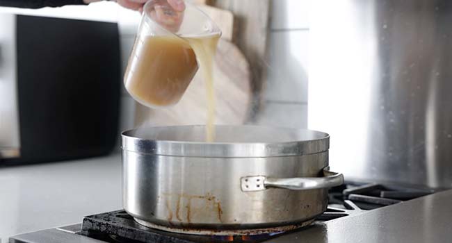 adding chicken stock to a pot