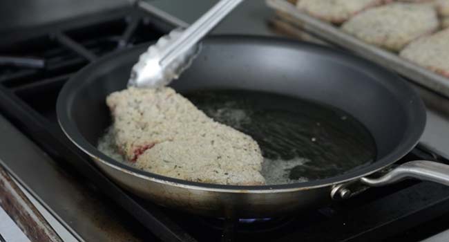 adding a breaded steak to a pan with oil