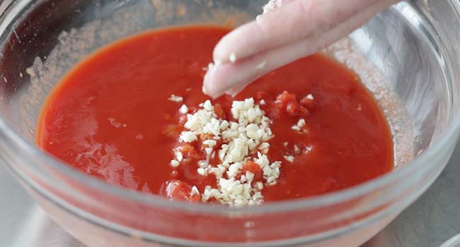 adding garlic to a bowl of tomatoes