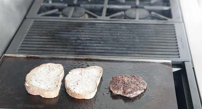 toasting bread on a griddle with a burger