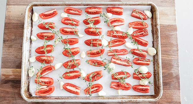 tomatoes on a sheet tray with garlic and thyme