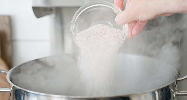 adding salt to a pot of boiling water