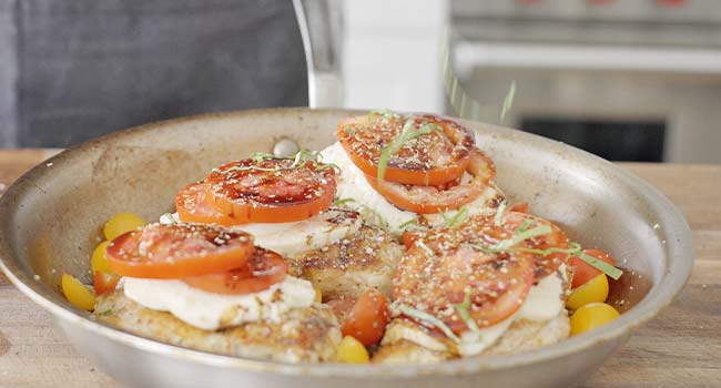 sprinkling herbs on chicken caprese