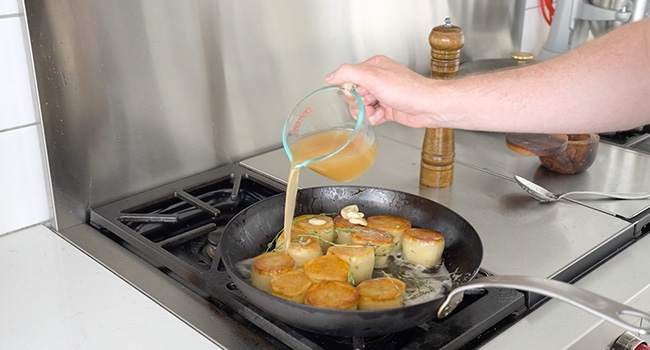 adding chicken stock to a pan of potatoes