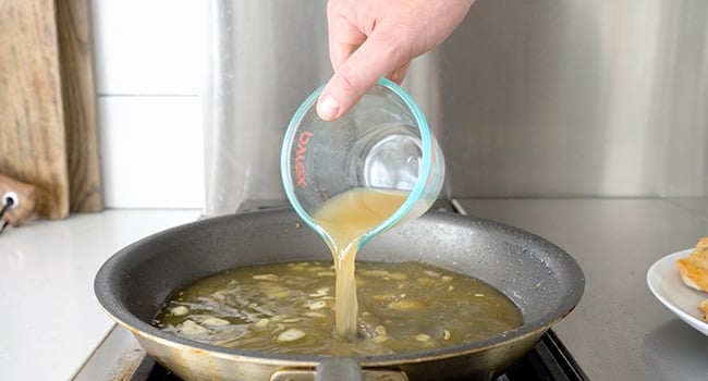 adding chicken stock to a pan