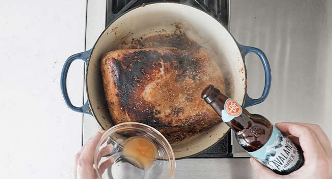 adding beer and vinegar to a pot with pork