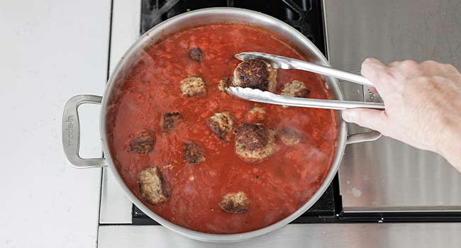 adding meatballs to tomato sauce