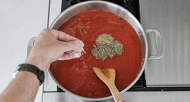 adding herbs and seasonings to tomato sauce