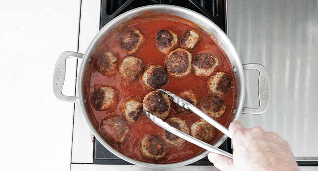 adding meatballs to tomato sauce